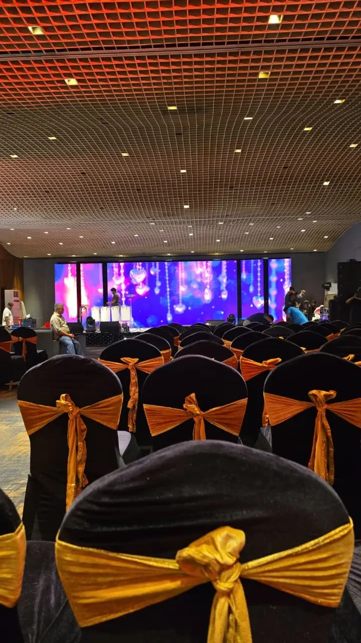 Banquet hall set with black chairs and gold sashes facing a lit LED stage